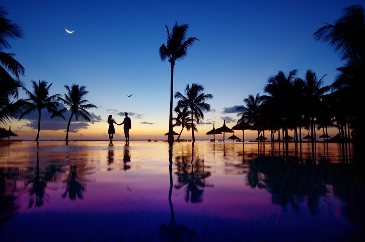 couple walking hand in hand by a pool in the sunset